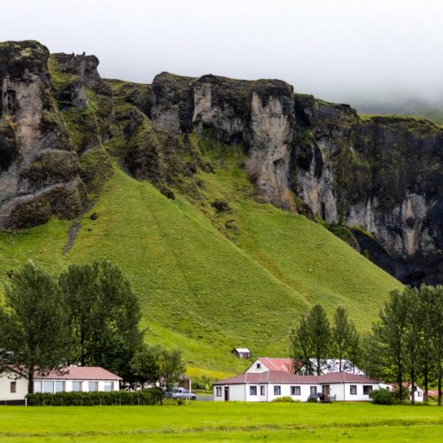 Lush green mountainside with white houses below, Iceland