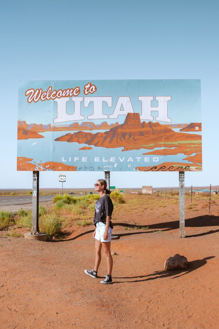 girl standing in front of the Utah state line sign