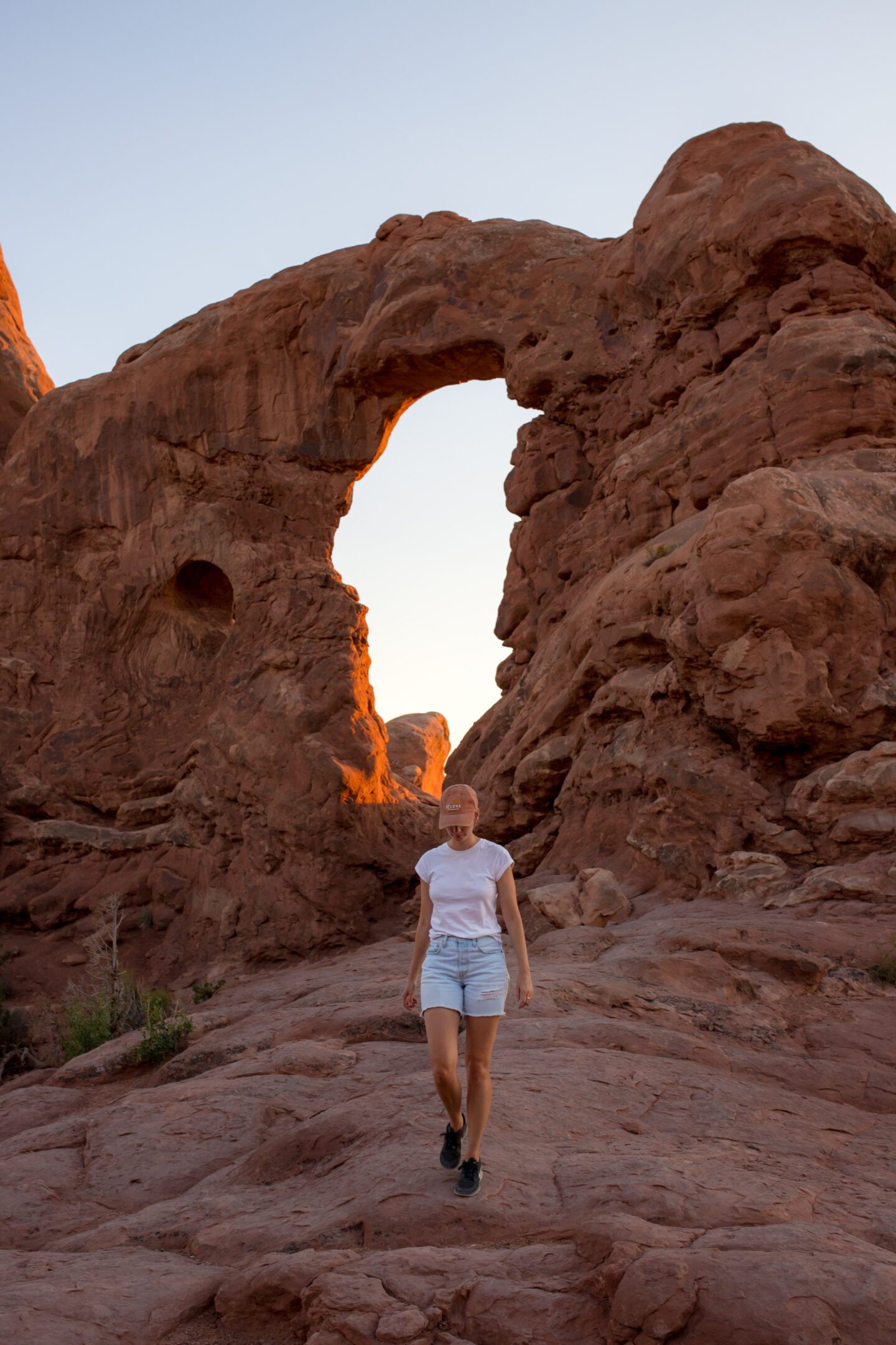 A girl walking down a rock hill in front of a large arched rock formation 
