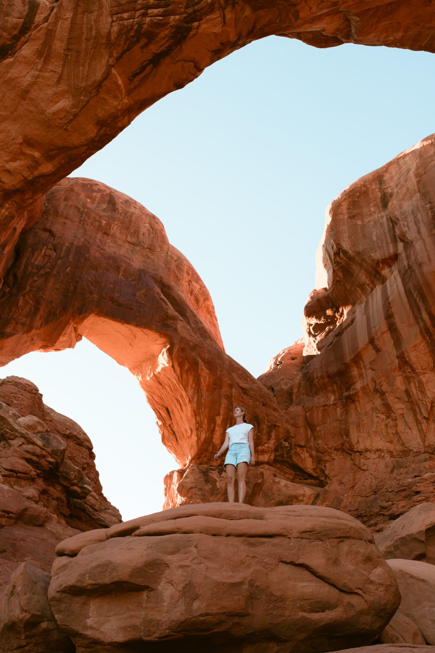 girl standing on a rock underneath a large rock archway, best arches in arches national park