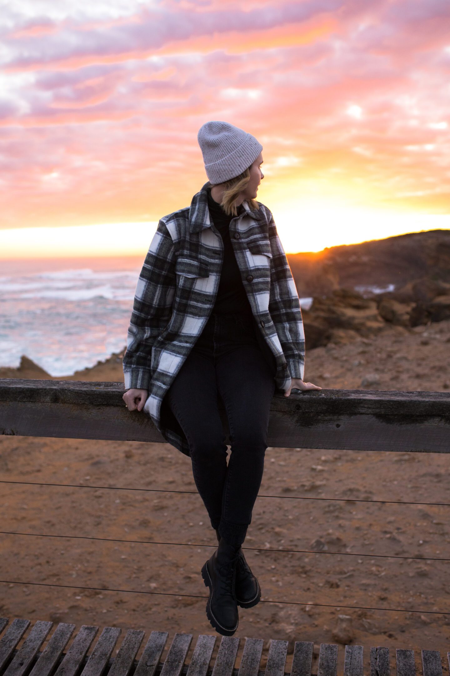 A girl perched on a fence looking at a colorful sunset, things to do in Warrnambool